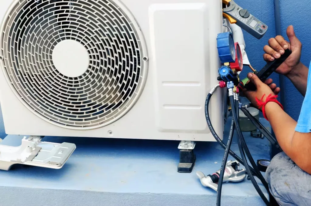 A person connecting a gauge set and clamp meter to the service ports of an outdoor air conditioning unit.
